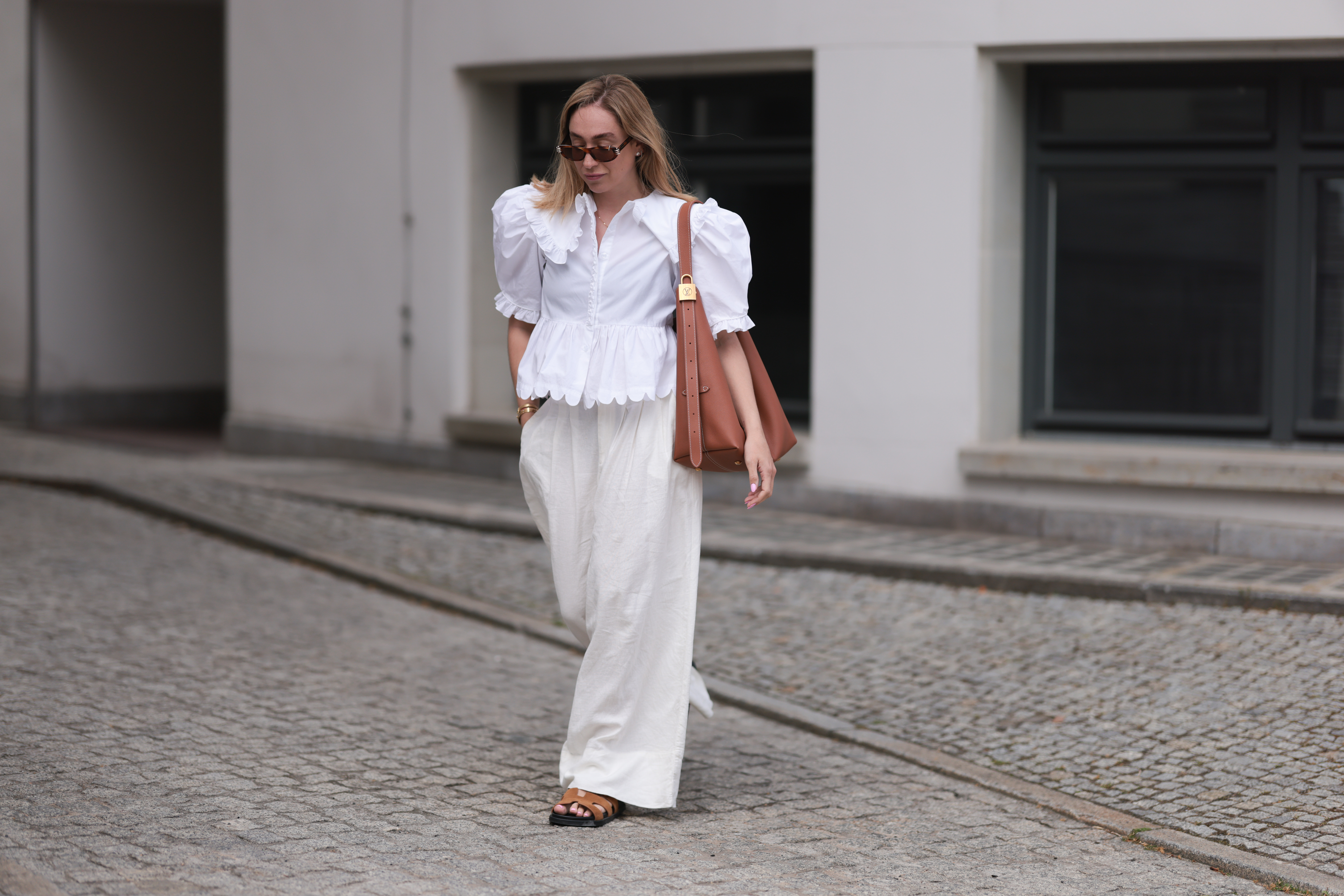 BERLIN, GERMANY - JUNE 11: Sonia Lyson is seen wearing sunglasses with havana frame from Givenchy, silver earrings, a golden necklace, a white blouse with puffed sleeves and ruffled details from Horror Vacui, cream-white wide linen pants from Zara, the “Low Key Hobo” bag in brown leather from Louis Vuitton and brown suede sandals from Hermès on June 11, 2024 in Berlin, Germany. (Photo by Jeremy Moeller/Getty Images)