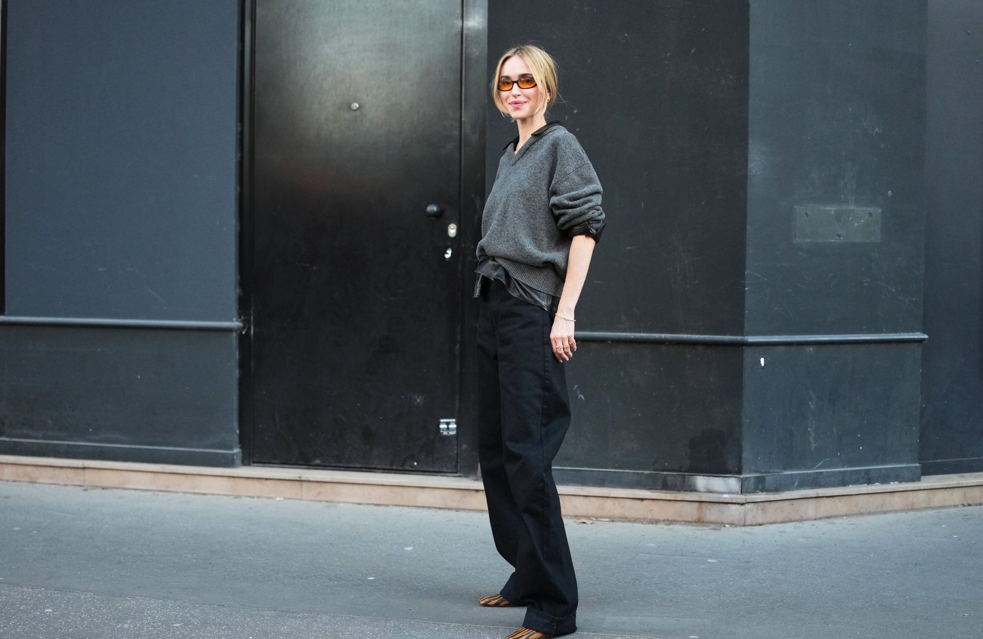 PARIS, FRANCE - MARCH 04: A guest wears blonde hair in a low bun, orange tinted sunglasses, a dark gray knit V neck wool sweater, a gold necklace, black wide leg balloon pants, a black leather with silver buckle belt, brown and black zebra print pattern leather pumps shoes, outside Acne Studios, during Paris Fashion Week - Womenswear Fall/Winter 2026/2027, on March 04, 2026 in Paris, France (Photo by Edward Berthelot/Getty Images)