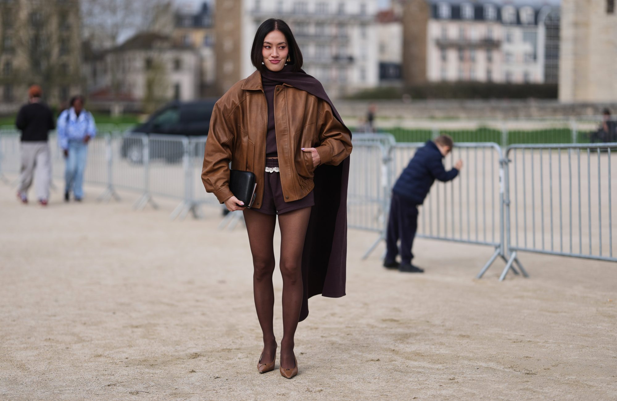 PARIS, FRANCE - MARCH 06: Tiffany Hsu wears black hair in a bob haircut, gold earrings, a brown leather oversized jacket, a dark brown knit turtleneck top with long scarf, dark brown fitted shorts, a black leather handbag, brown tights, dark brown leather pointed pumps shoes, outside Loewe, during Paris Fashion Week - Womenswear Fall/Winter 2026/2027, on March 06, 2026 in Paris, France (Photo by Edward Berthelot/Getty Images)