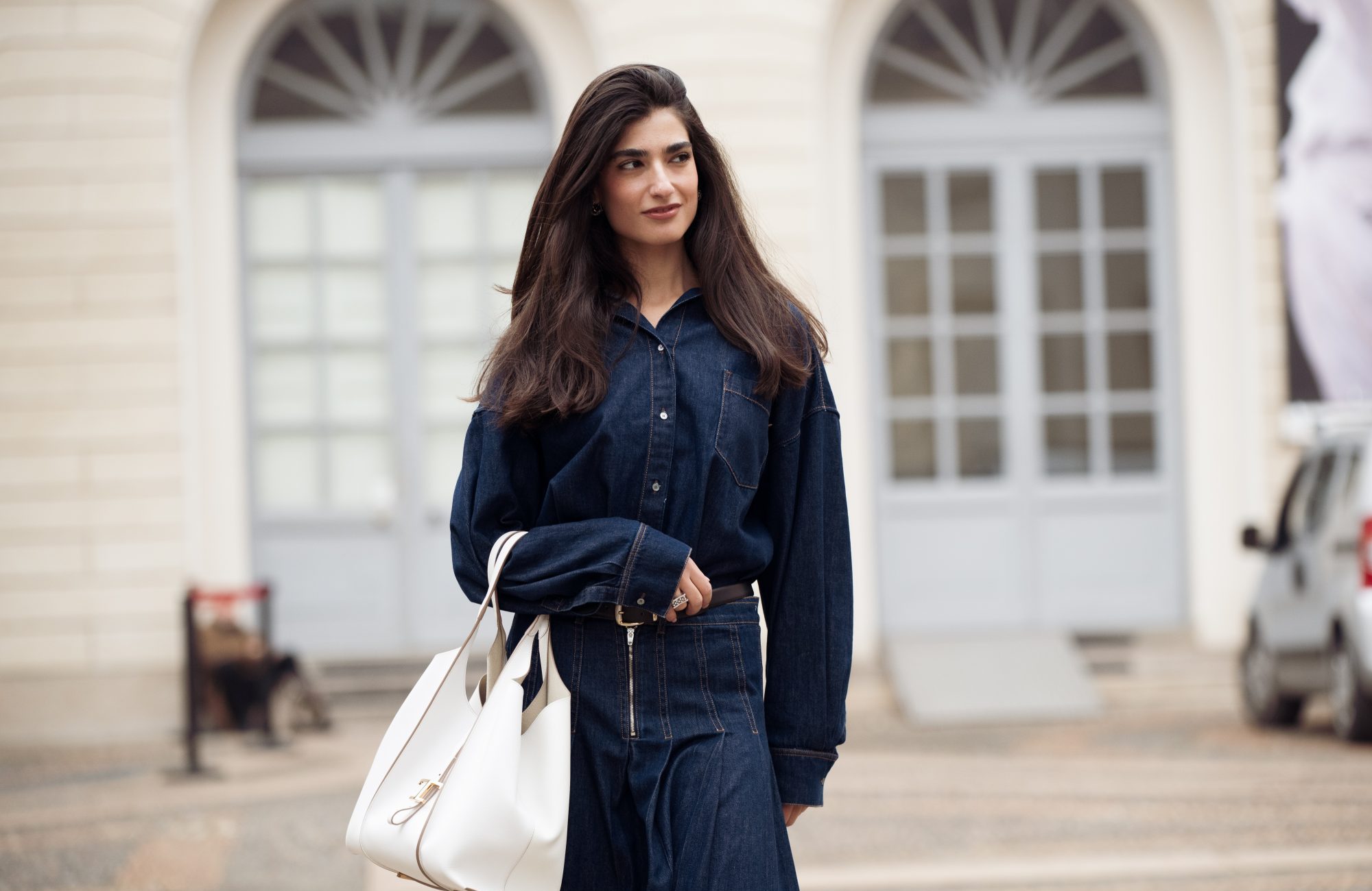 MILAN, ITALY - FEBRUARY 27: A guest wears a dark blue denim long-sleeve shirt dress with contrast stitching and a front zipper detail, cinched at the waist with a black leather belt, styled with a large white leather tote bag outside Tod's show during the Milan Fashion Week - Womenswear Fall/Winter 2026/2027 on February 27, 2026 in Milan, Italy. (Photo by Raimonda Kulikauskiene/Getty Images)