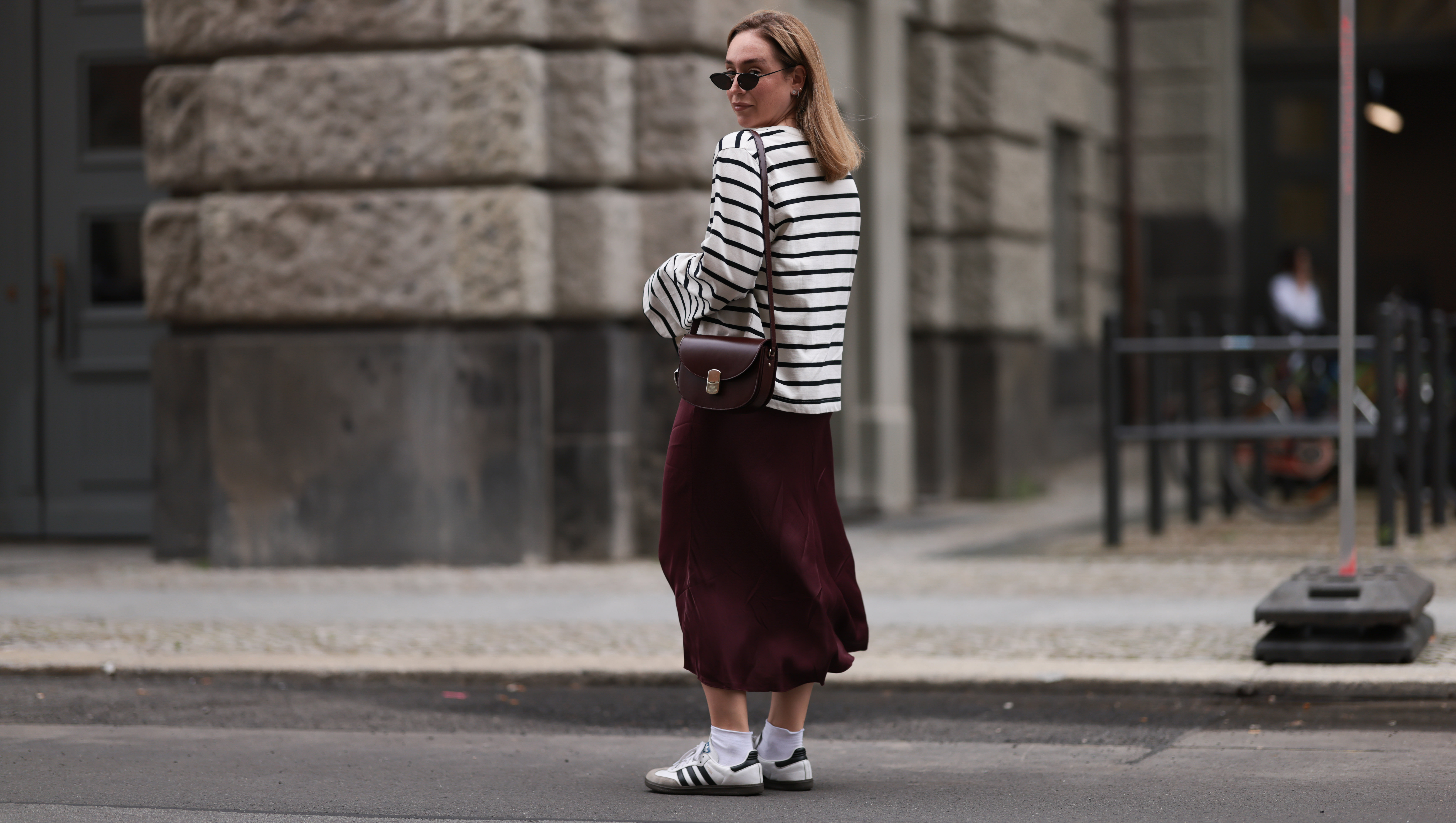 BERLIN, GERMANY - JULY 13: Sonia Lyson is seen wearing several silver and golden earrings and ear studs; a black, oval sunglasses with filigree metal frame from Yves Saint Laurent; a white sweatshirt with black stripes and loose fit from Zara; a burgundy satin midi skirt from Zara; a burgundy leather bag from Sézane; white socks and white Samba sneakers from Adidas on July 13, 2024 in Berlin, Germany. (Photo by Jeremy Moeller/Getty Images)