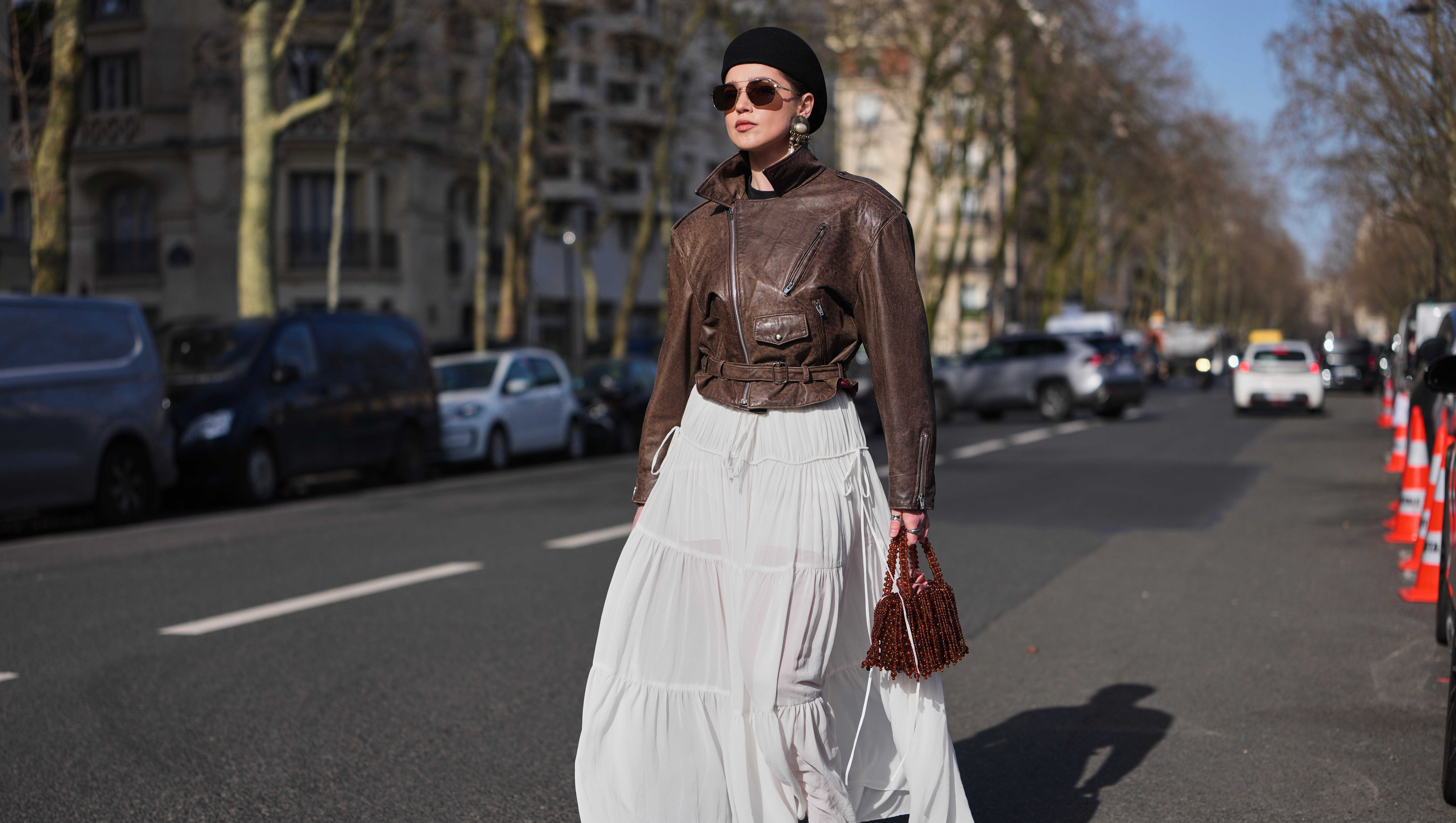 PARIS, FRANCE - MARCH 05: A guest wears a black felt pillbox hat, brown hair, brown tinted aviator sunglasses, a dark brown leather belted biker zipper jacket, a white chiffon tiered long skirt, a dark brown fringed beaded / pearls handbag, dark brown leather platform soles / high heels shoes, outside Chloe, during Paris Fashion Week - Womenswear Fall/Winter 2026/2027, on March 05, 2026 in Paris, France (Photo by Edward Berthelot/Getty Images)