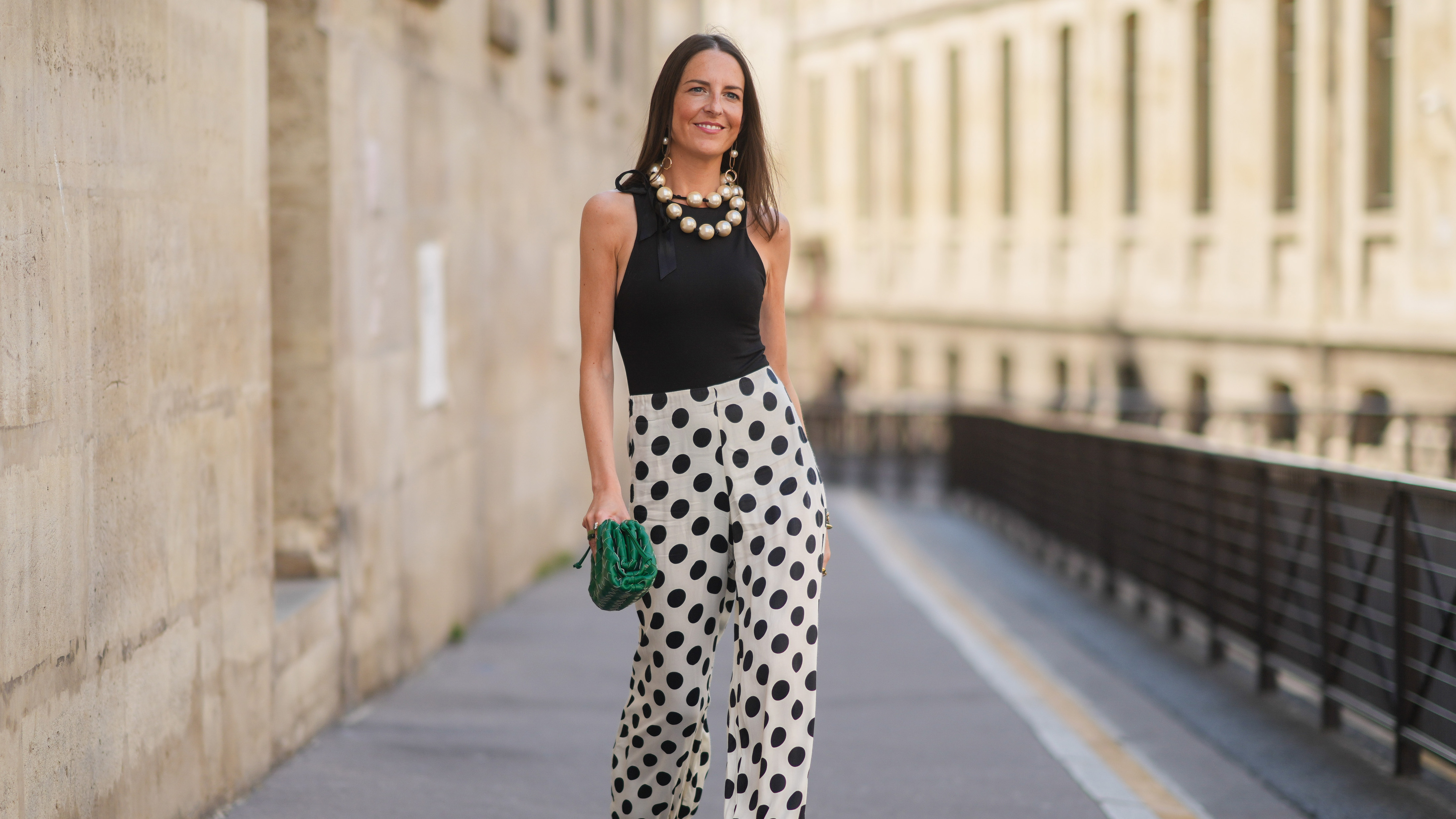 PARIS, FRANCE - JUNE 09: Alba Garavito Torre wears a gold and pearl earrings, a large pearls necklace, a black tank-top, a white with black polka dots puffy pants, a green shiny braided leather Bottega Veneta handbag, a gold Love bracelet from Cartier, gold bracelets, gold rings, black suede strappy pumps heels shoes, on June 09, 2021 in Paris, France. (Photo by Edward Berthelot/Getty Images)