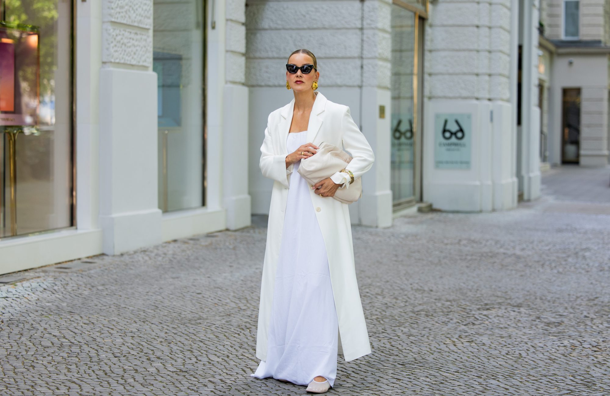 BERLIN, GERMANY - JULY 05: Tina Haase wears Gant white Maxi coat, Nakd white maxi dress, Arket mesh flats, Arket cream leather clutch bag, Joseph black Cateye Sunglasses on July 05, 2025 in Berlin, Germany. (Photo by Christian Vierig/Getty Images)