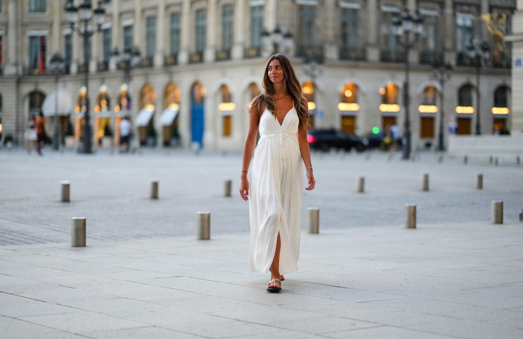 Amanda Derhy wears earrings, a white summer maxi pleated slit off-shoulder dress, sandals shoes , during a street style fashion photo session, on August 20, 2022 in Paris, France.