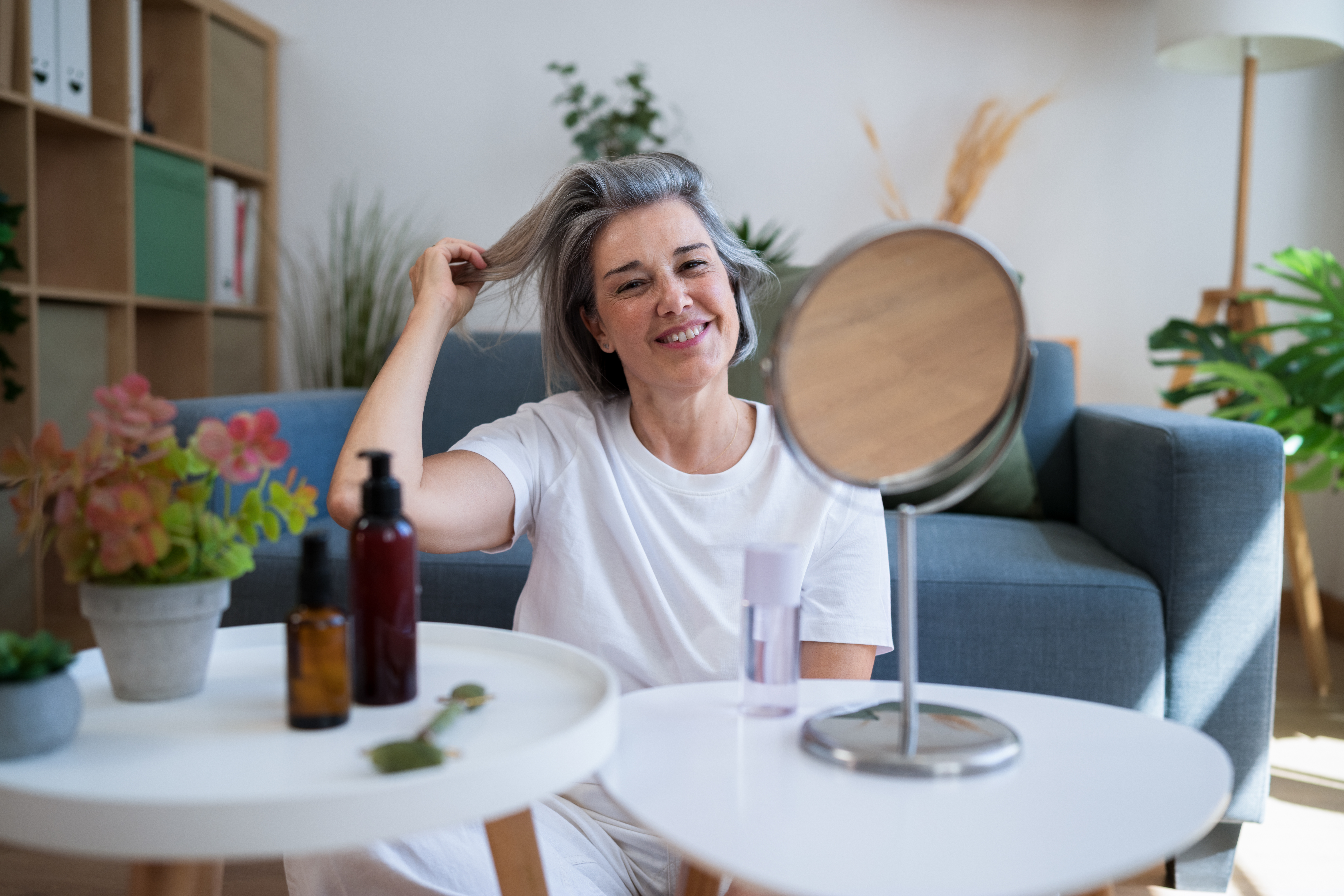 Smiling woman practicing beauty routine with mirror in home living room