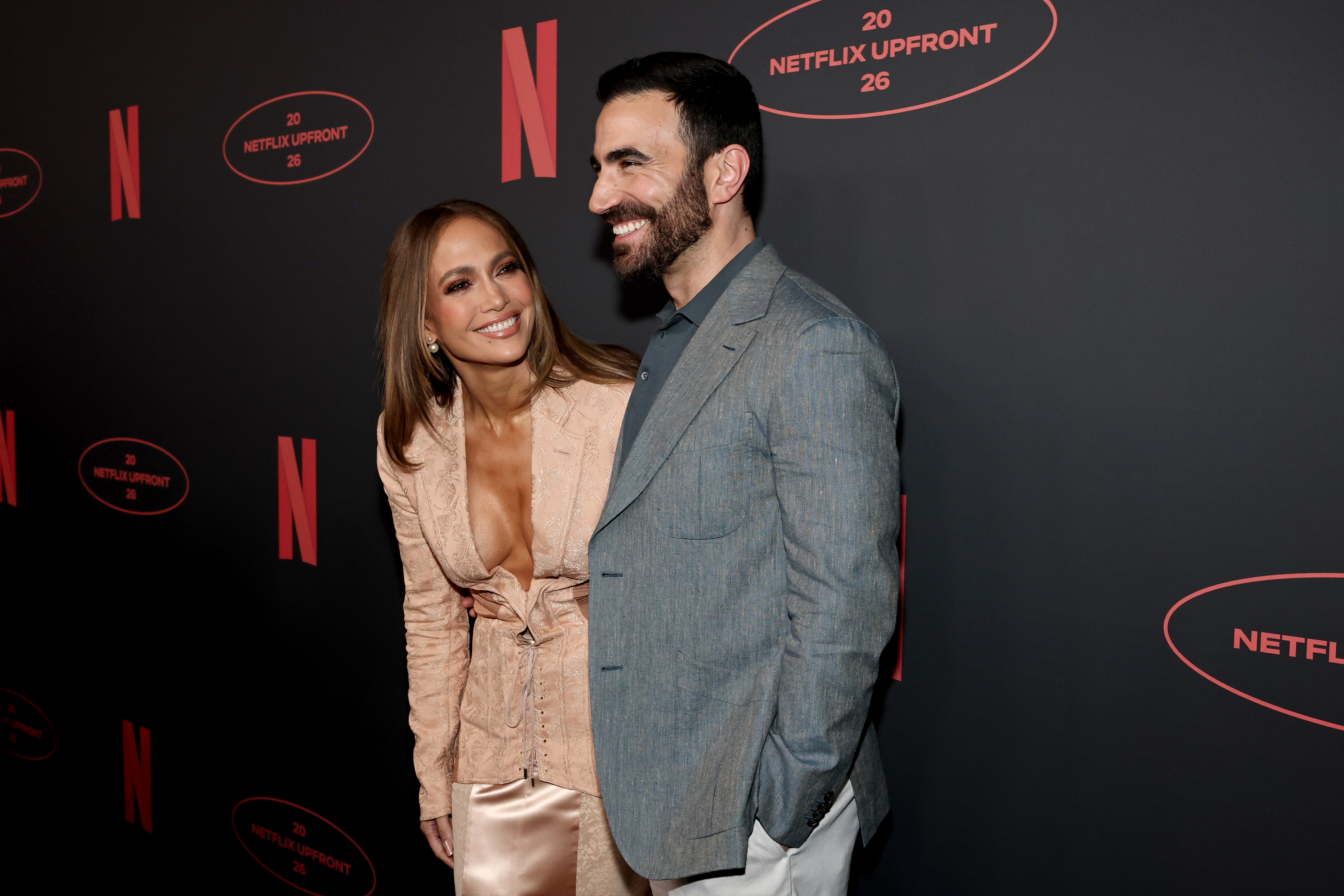 Jennifer Lopez and Brett Goldstein smiling together on a red carpet.