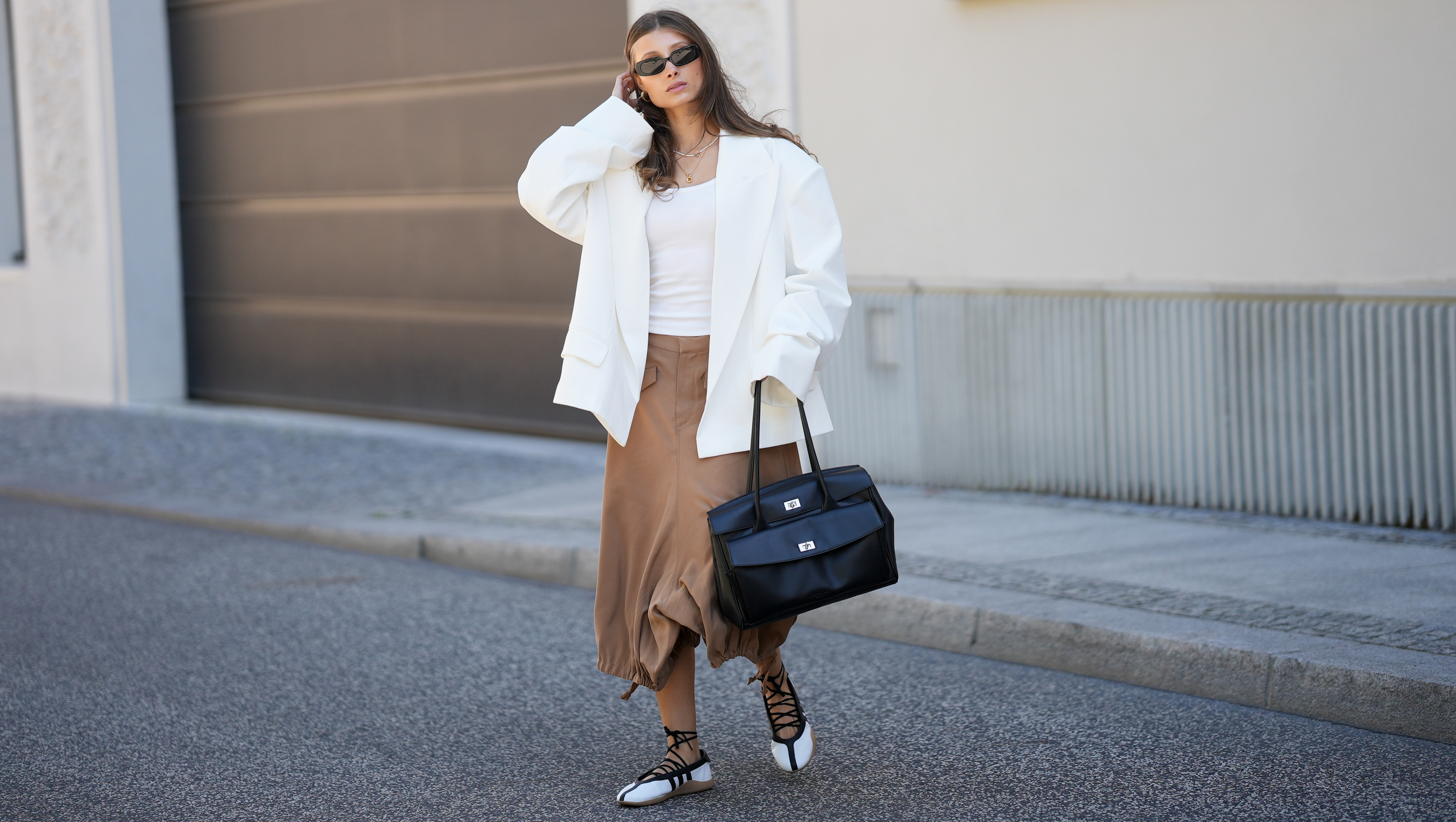 BERLIN, GERMANY - MAY 27: Lisa Mottl is seen wearing an off-white double-breasted oversized blazer with sharp wide peak lapels, padded shoulders, long sleeves, two parallel rows of matching fabric-covered buttons and classic horizontal flap pockets from Bazhane; a white fitted top from Zara; camel brown cargo-inspired cropped capri length trousers with belt loops, angled flap pockets, wide fluid legs and adjustable drawstring toggle hems creating a gathered balloon-like silhouette from Zara; off-white leather "Taekwondo Mei" ballet flats featuring iconic contrast black stripes, a flexible gum sole and delicate wrap-around ankle laces from Adidas; a black "Archive Gloria II Satchel L" large shoulder bag crafted from soft calf leather with a flap main compartment, an applied front pocket, twist lock closures, two top handles, side snap buttons for width adjustment and logo embossing on the front from Liebeskind Berlin; necklaces; "Olsen" sunglasses with a slim rectangular frame crafted from black acetate and smoke grey lenses from Vehla; her brown hair is worn loose with a center part; with natural make up on May 27, 2026 in Berlin, Germany. (Photo by Moritz Scholz/Getty Images)