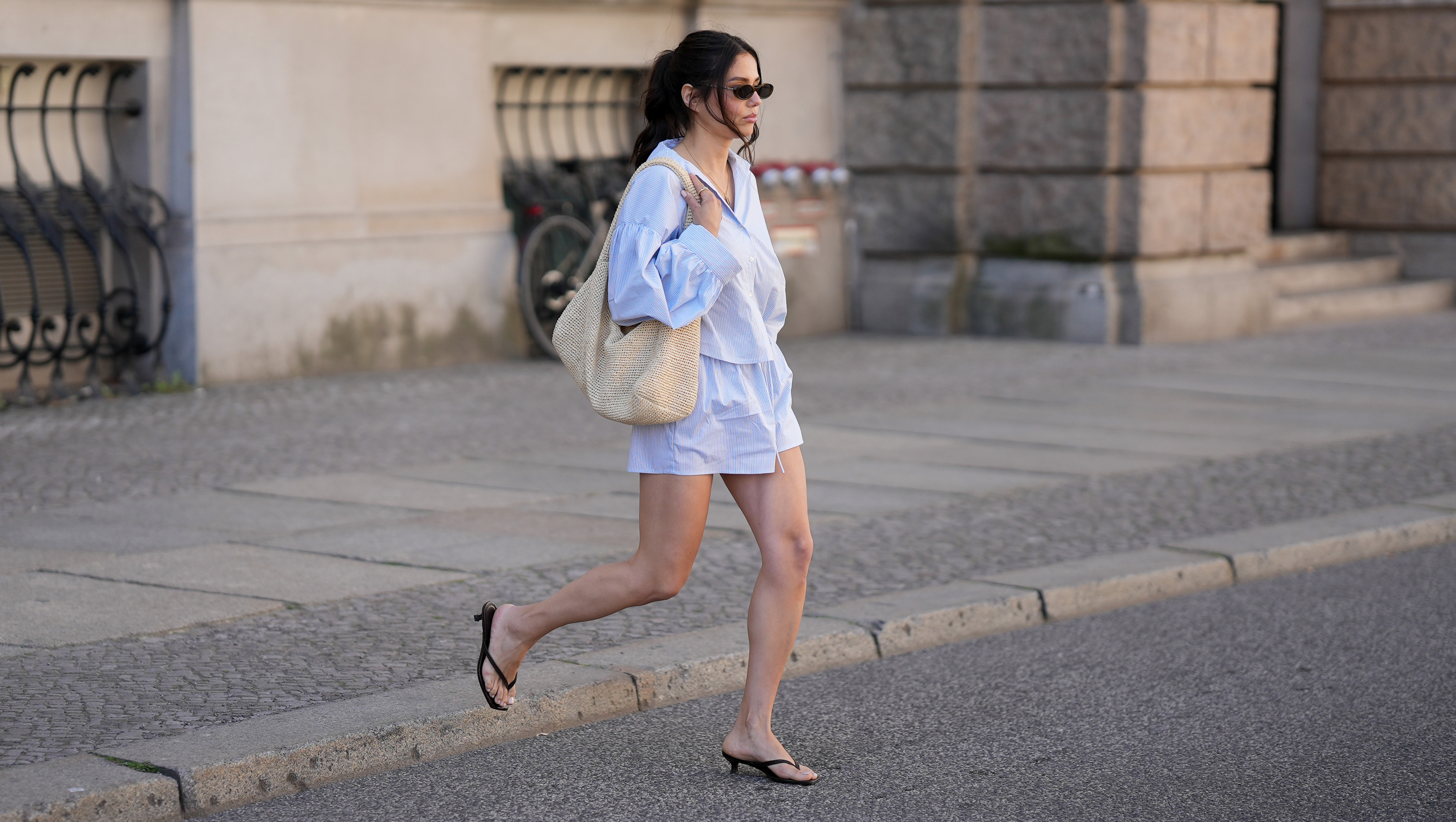 BERLIN, GERMANY - MAY 27: Aylin Seng&uuml;l is seen wearing a blue-and-white striped oversized two-piece set consisting of a cropped button-up shirt with voluminous sleeves and matching shorts by Set Dish; black kitten-heel thong sandals by H&M; a large raffia shoulder bag by COS; narrow rectangular sunglasses by Chanel; gold jewelry consisting of rings and a delicate necklace; natural makeup; her dark brown hair is styled in a relaxed low updo with loose face-framing strands on May 27, 2026 in Berlin, Germany. (Photo by Moritz Scholz/Getty Images)