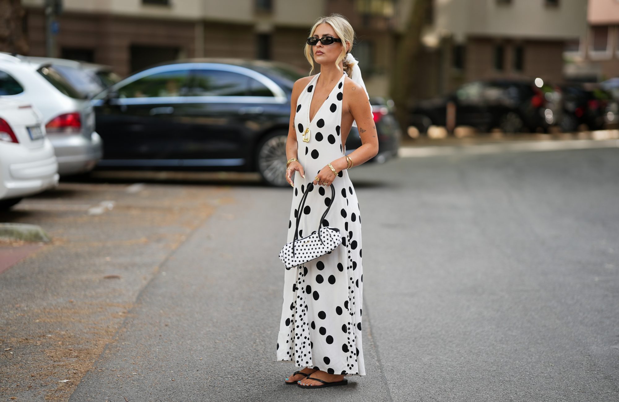 FRANKFURT AM MAIN, GERMANY - JUNE 3: Julia Kammerer is seen wearing a white cotton halter maxi dress with black polka dot print, a deep V neckline and a flowing silhouette from SUSMIES; a white scarf with black polka dot print worn in the hair from Fraas; black flat sandals from Havaianas; a turquoise pedicure visible on the toes; a white leather top handle bag with black polka dot print, rounded shape and black handles from WEAT; gold tone hoop earrings, layered necklaces, bracelets and rings from H&M, My Jewellery, Pandora, Scandivv; black rectangular acetate sunglasses with dark tinted lenses from Weller Eyewear; her blonde hair is worn loose with a center part; with natural make up on June 3, 2026 in Frankfurt am Main, Germany. (Photo by Moritz Scholz/Getty Images)