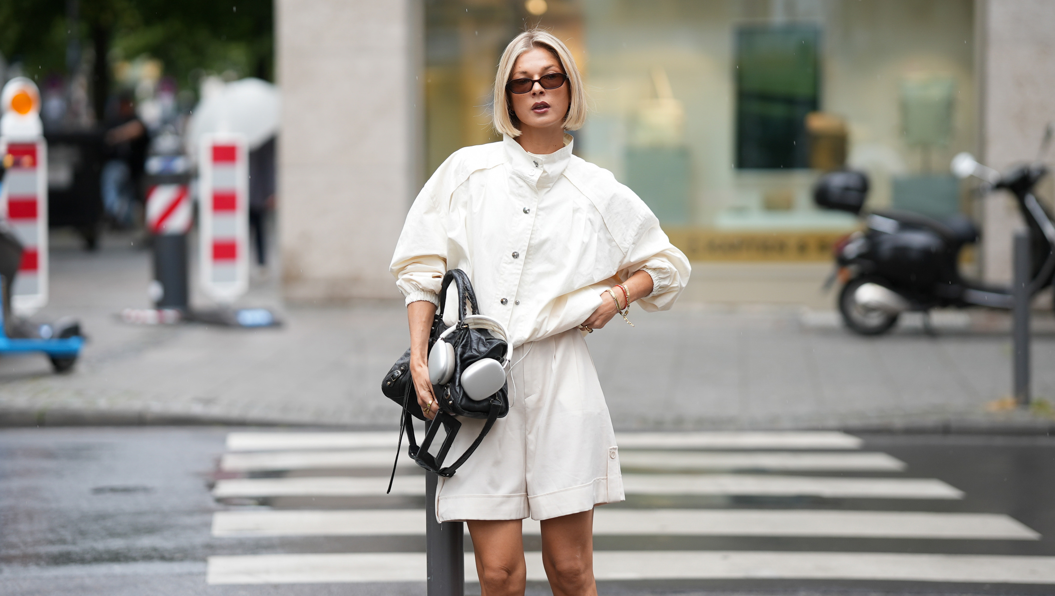 FRANKFURT AM MAIN, GERMANY - JUNE 3: Laura Wittek is seen wearing a white cotton oversized cropped jacket with a high collar, button front closure and gathered sleeves from Laura Wittek x Na-kd; white cotton shorts with a straight silhouette and elastic waist detail from Massimo Dutti; a black leather compact shoulder bag with a curved silhouette and silver tone hardware from Balenciaga; silver bracelets and rings; rectangular acetate sunglasses with dark tinted lenses from Corlin Eyewear; silver Apple headphones; her blonde hair is worn in a sleek bob with a center part; with natural make up on June 3, 2026 in Frankfurt am Main, Germany. (Photo by Moritz Scholz/Getty Images)