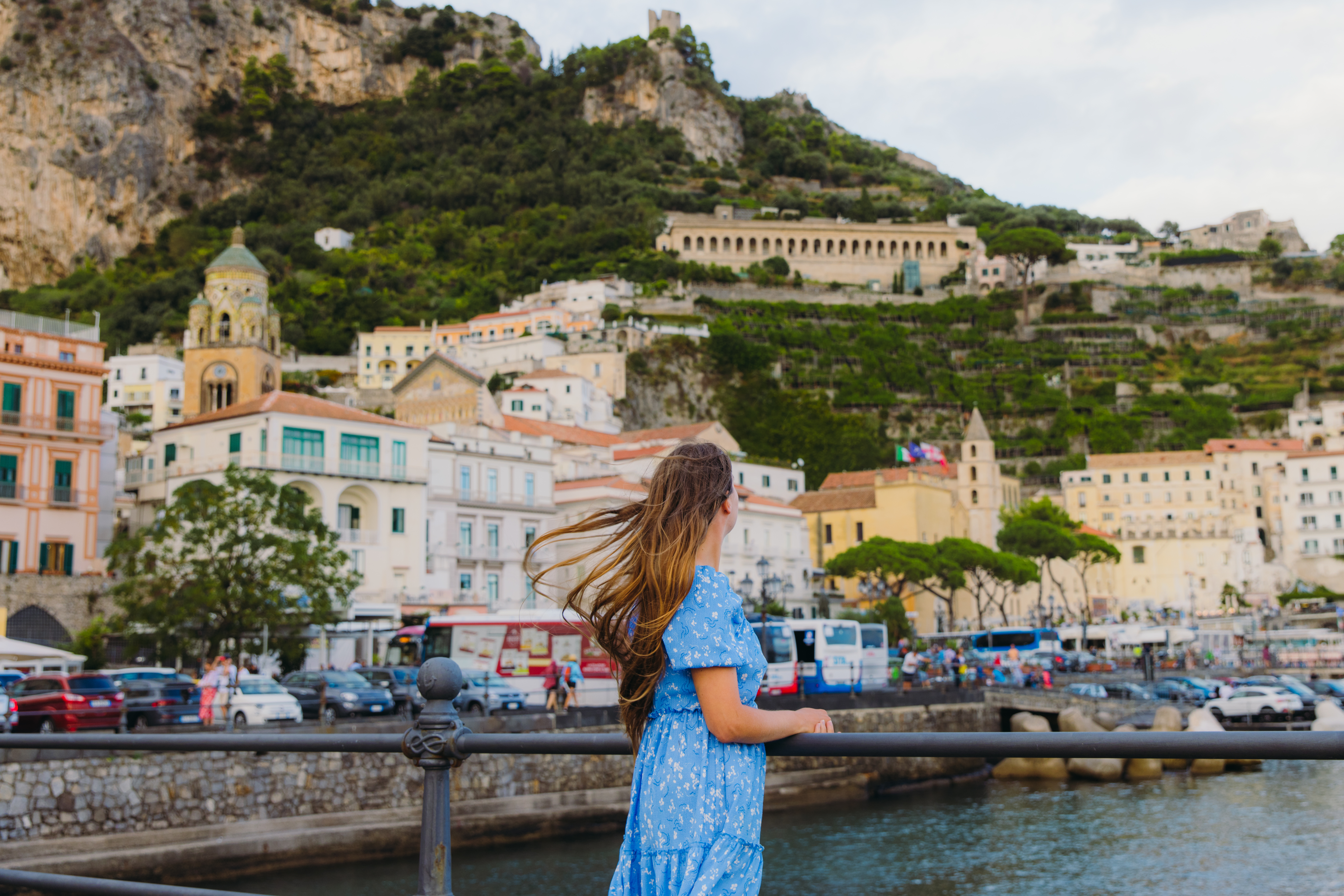 Side view of smiling female tourist with long hair exploring Amalfi Coast and walking the authentic streets with colourful houses by the sea