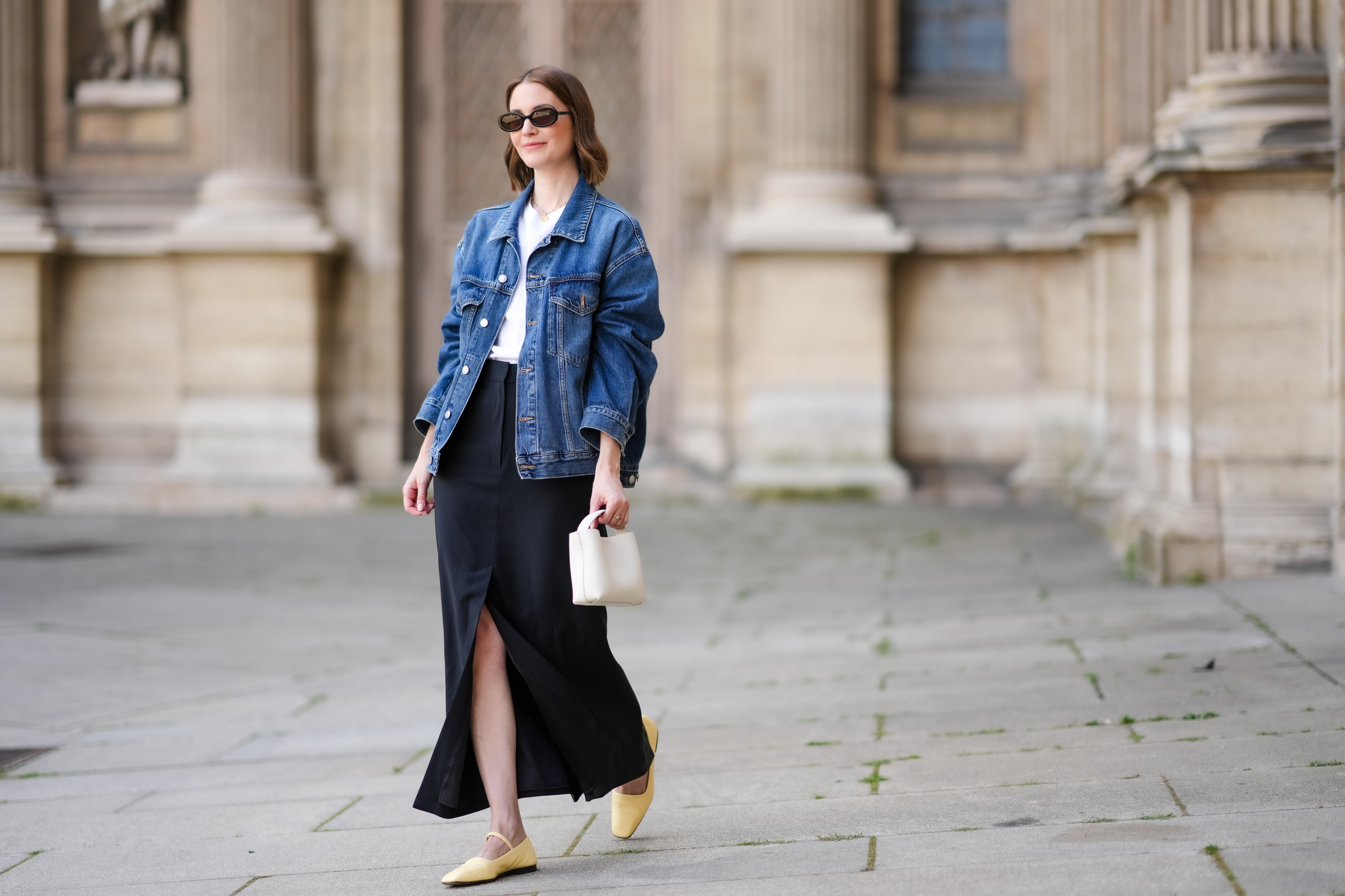PARIS, FRANCE - MAY 25: Marissa Cox wears an Arket black skirt, an Arket white t-shirt, a blue oversize Agolde denim jacket, ATP Atelier pale pastel yellow flats / shoes, a white Arket leather bag, Jimmy Fairly x Reformation sunglasses, and Alighieri necklace, during a street style fashion photo session, on May 25, 2024 in Paris, France. (Photo by Edward Berthelot/Getty Images)