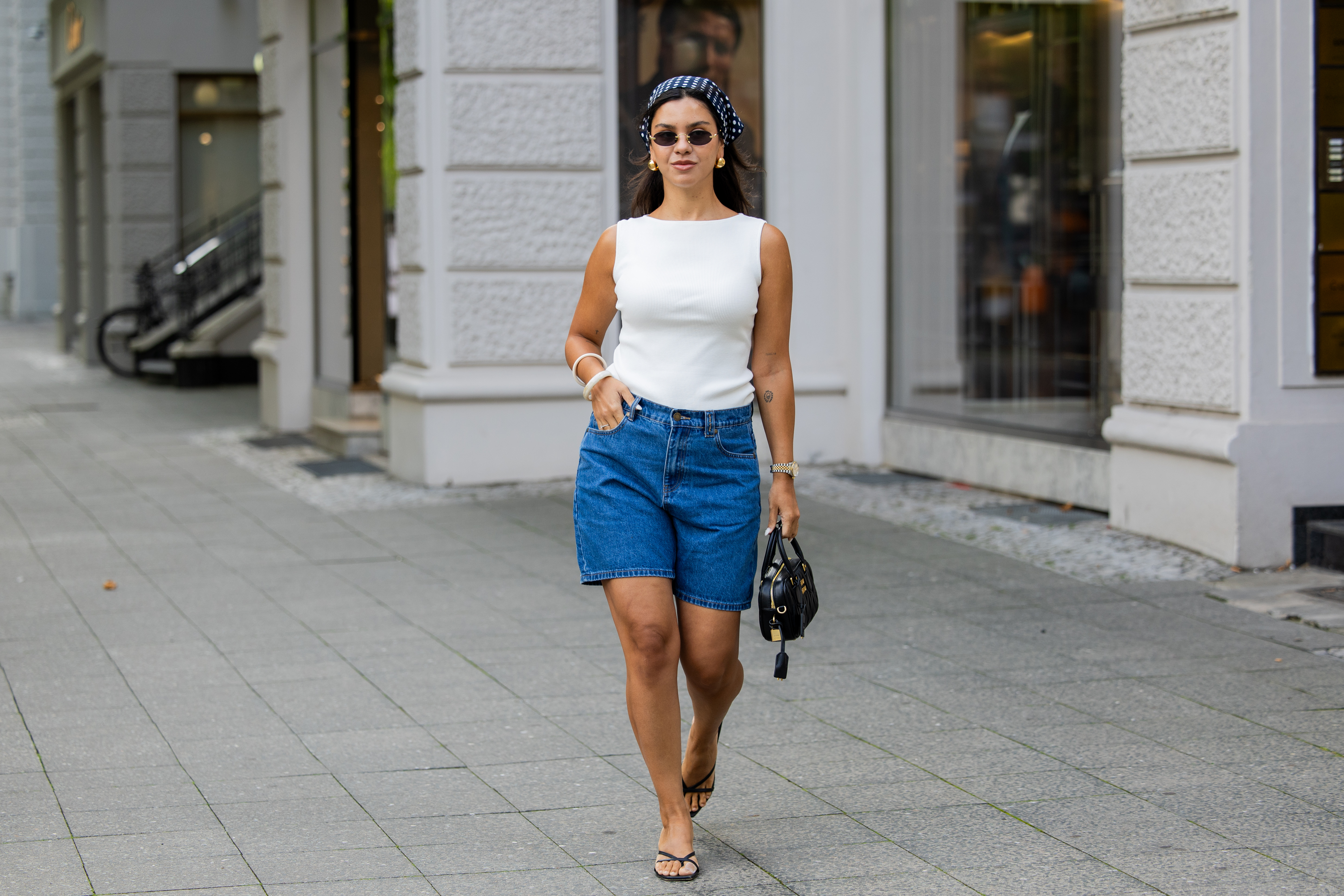 BERLIN, GERMANY - AUGUST 03: Bella Emar wears blue Polo Club Jeans Shorts & white Top, H&M sandals, Miu Miu Sunglasses & black Miu Miu bag, blue head scarf on August 03, 2025 in Berlin, Germany. (Photo by Christian Vierig/Getty Images)