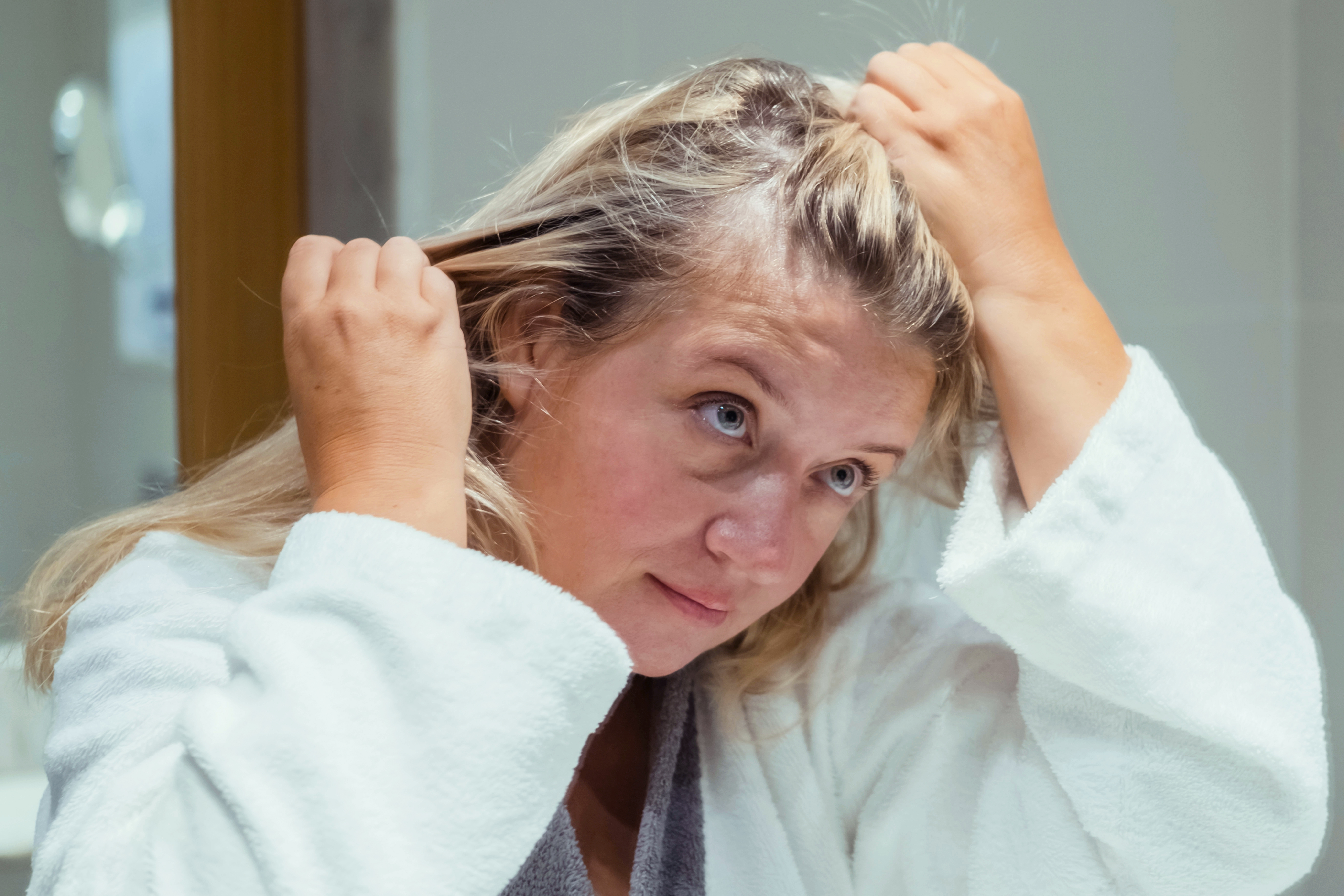 Blond woman applies oil to her hair with massage. Beauty caring for scalp and hair.