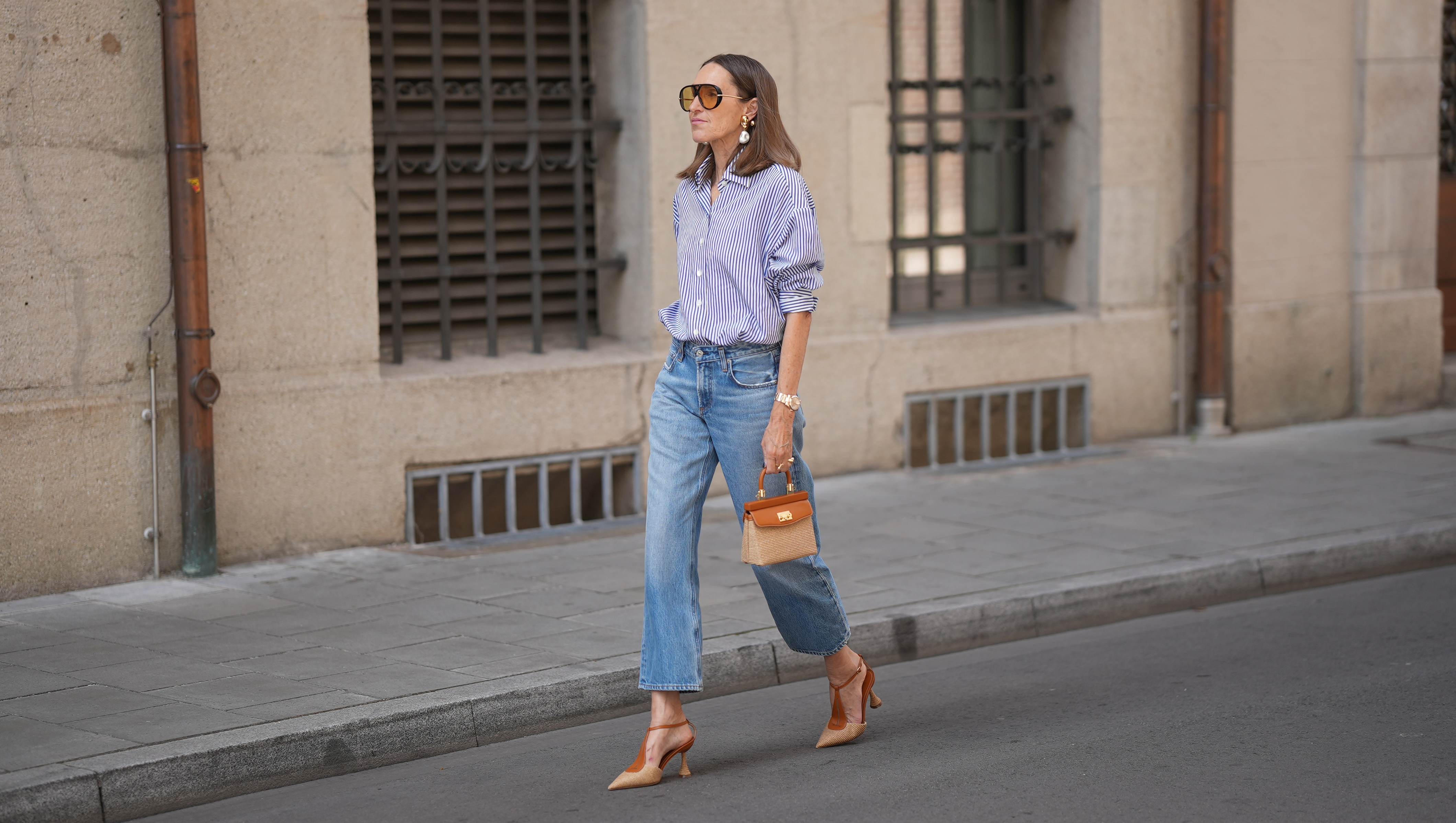 MUNICH, GERMANY - JUNE 8: Annette Weber is seen wearing a blue and white striped cotton oversized shirt with a loose silhouette from Glamometer x Seidensticker; light blue denim straight leg jeans with a cropped silhouette from Citizens of Humanity; brown suede pointed toe slingback shoes with a low heel from Rodo Firenze; a small brown and beige woven leather top handle bag with a compact silhouette, gold tone hardware and structured shape from Rodo Firenze; pearl drop earrings from Manuela Fumagalli, a rosé gold "Day Date Everose" wristwatch from Rolex; black nail polish; oversized oval acetate sunglasses with brown tinted lenses from Bottega Veneta; her brown hair is worn loose with a center part; with natural make up on June 8, 2026 in Munich, Germany. (Photo by Moritz Scholz/Getty Images)
