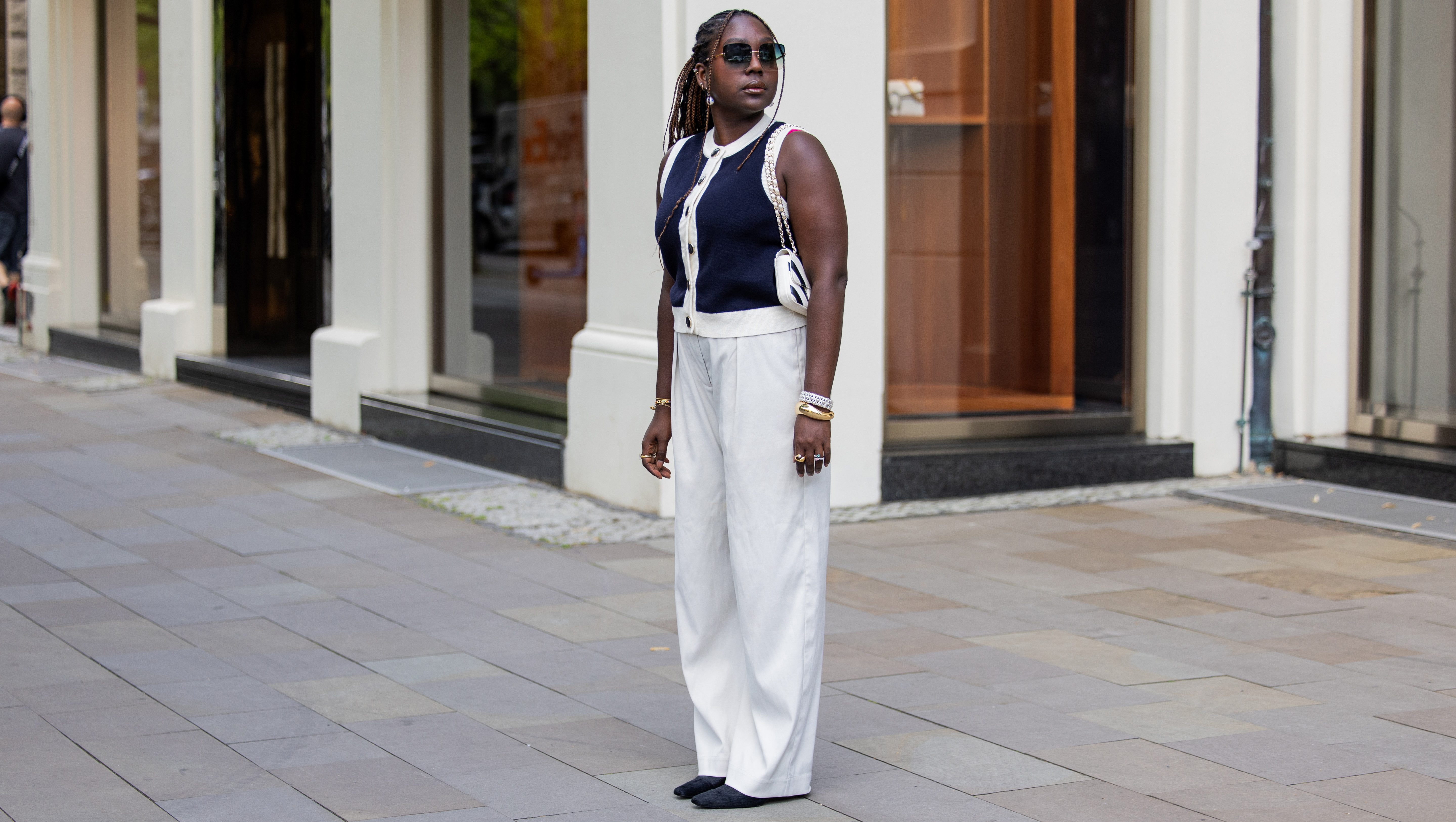 BERLIN, GERMANY - JULY 02: Lois Opoku wears navy cardigan sleeveless vest Sezane, white pants Monki, heels H&M Studio, sunglasses Kate Spade, black white Chanel bag, bracelet during the Berlin Fashion Week Spring/Summer 2026 at on July 02, 2026 in Berlin, Germany. (Photo by Christian Vierig/Getty Images)