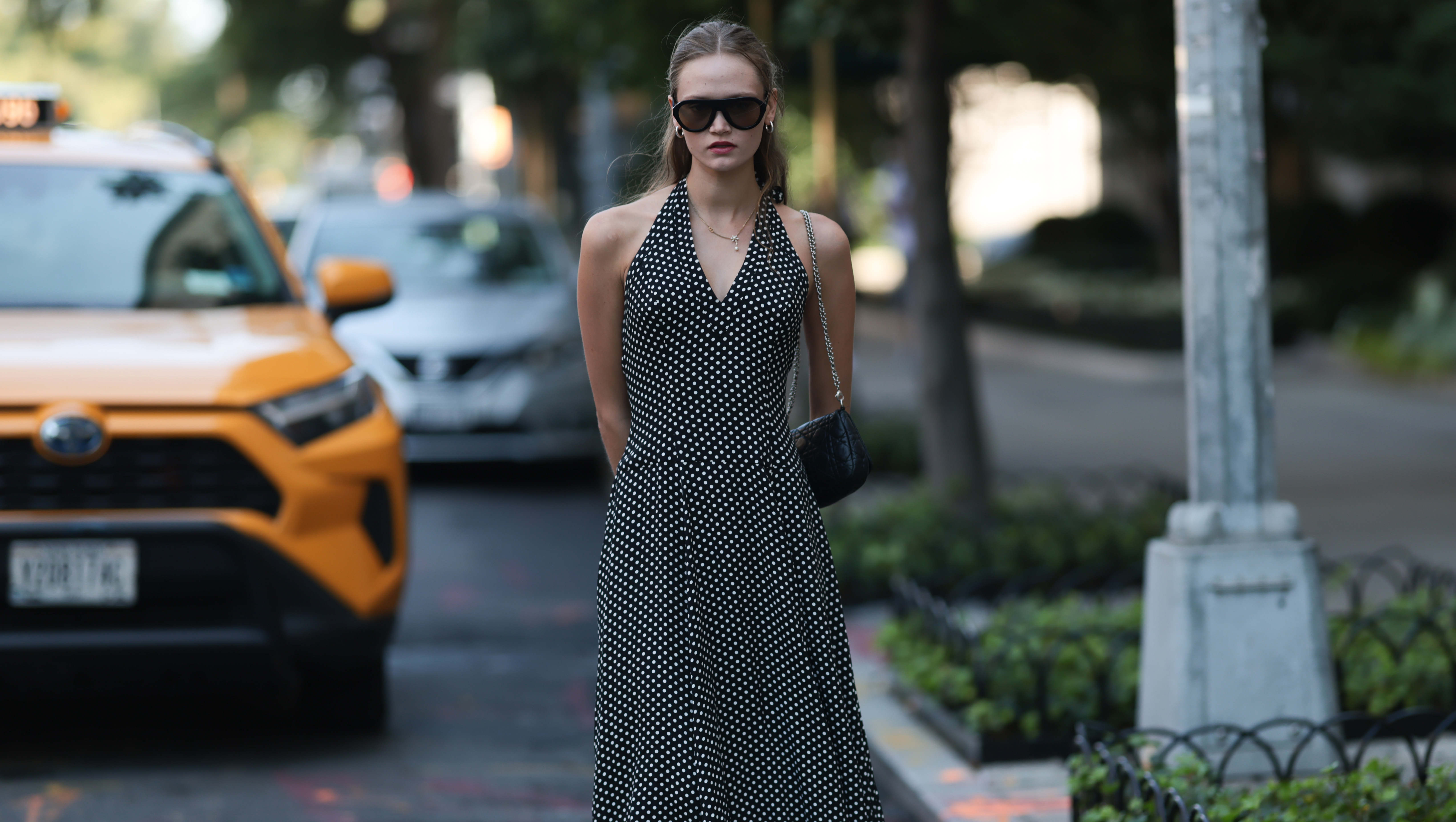 NEW YORK, NEW YORK - SEPTEMBER 14: A blond-haired woman seen wearing a black long dress with white dots, black leather handbag with a silver chain, black sunglasses, silver earrings and a necklace chain, rings and black slip in shoes outside Vettese show during New York Fashionweek on September 14, 2025 in New York City. (Photo by Jeremy Moeller/Getty Images)