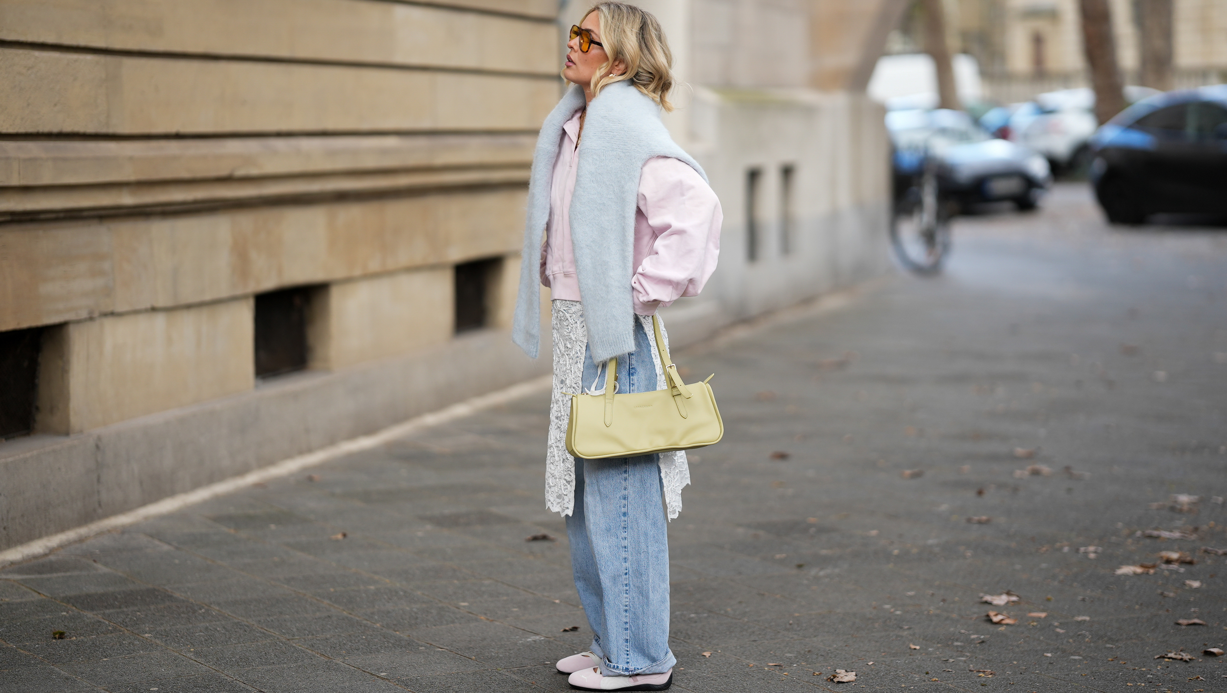 FRANKFURT AM MAIN, GERMANY - MARCH 26: Julia Kammerer is seen wearing a light pink silk shirt with a pointed collar and a partial button placket from Lily Silk; a baby blue knit sweater draped around her shoulders from ASOS; light blue wide leg denim jeans with a relaxed fit from Levi's; a white floral lace wrap skirt overlay featuring delicate scalloped edges from NA-KD; light pink and white leather "Speedcat Ballet Sneaker" with a thin rubber sole from Puma; a light green leather "L Looong" handbag with a horizontal silhouette and dual top handles from Longchamp; her jewelry includes chunky gold hoop earrings and gold tone stacked rings worn across multiple fingers from H&M, Pandora and My Jewellery; orange tinted aviator sunglasses with a thin black frame from Bershka; her blonde hair is styled in loose waves with a center part on March 26, 2026 in Frankfurt am Main, Germany. (Photo by Moritz Scholz/Getty Images)