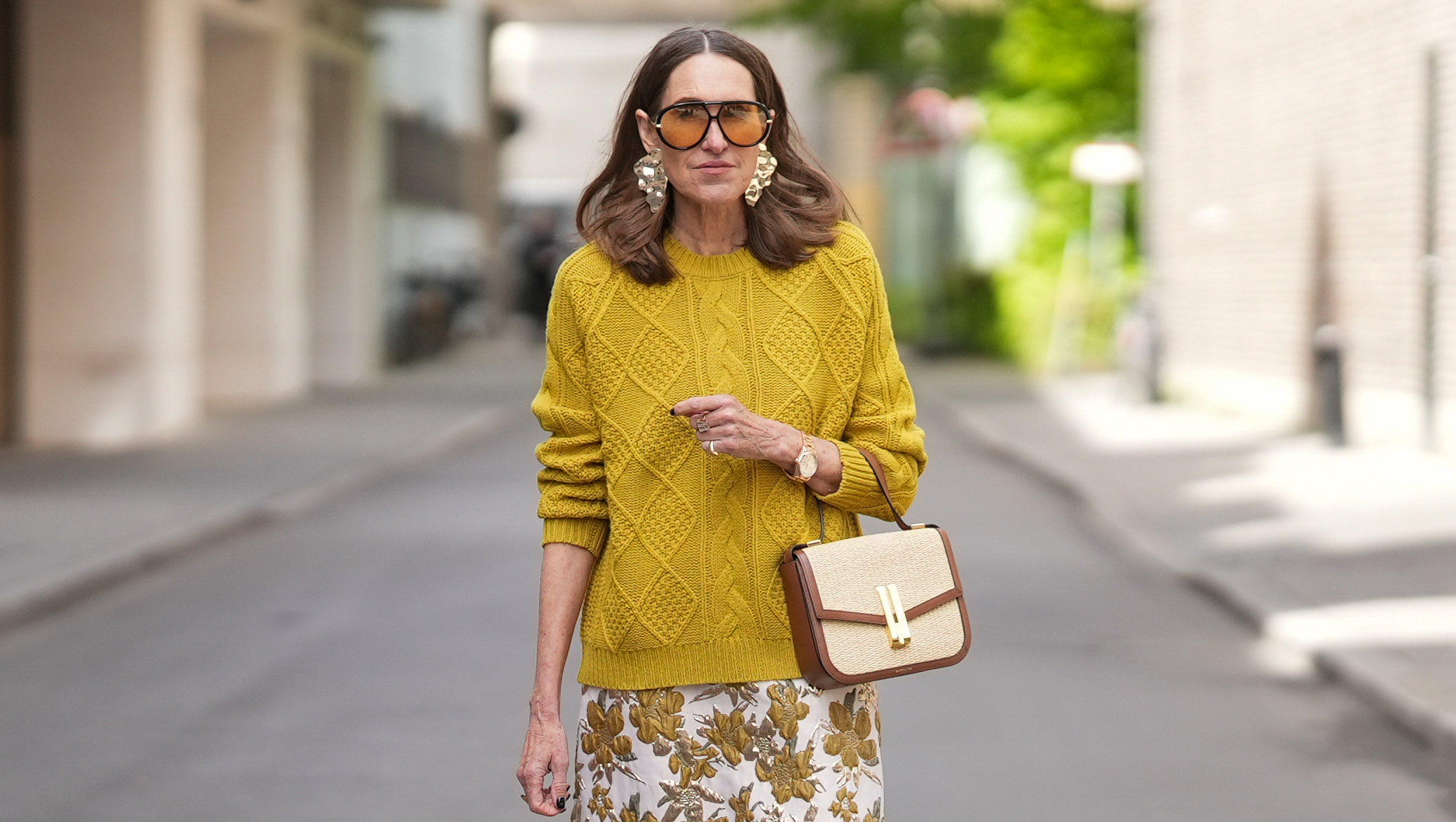 MUNICH, GERMANY - APRIL 28: Annette Weber is seen wearing a mustard yellow wool knit sweater with a relaxed fit, ribbed crew neck, cuffs and hem and cable knit texture from Allude; a white cotton midi skirt with a straight silhouette and gold and brown floral print from TT Stories; a medium sized beige raffia and brown leather “Vancouver” shoulder bag with envelope flap top, double bar gold toned lock from DeMellier; gold tone statement drop earrings, a Rolex Day-Date 36 Everose rose gold with Oyster bracelet; multiple gold rings; dark nail polish; oversized aviator acetate sunglasses with orange tinted lenses from Bottega Veneta; her medium brown hair is worn loose in soft waves with a center part; with natural make up on April 28, 2026 in Munich, Germany. (Photo by Moritz Scholz/Getty Images)