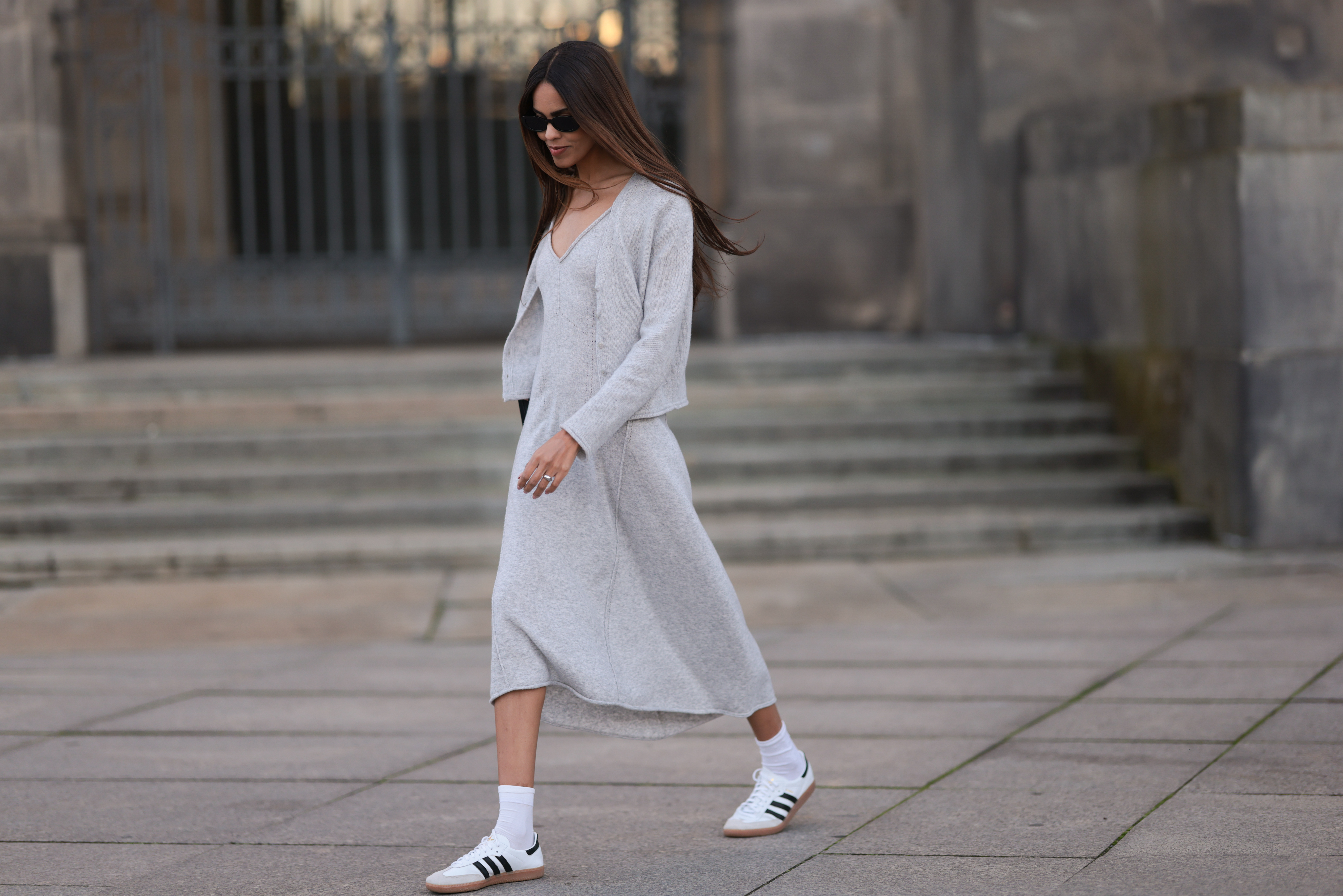 Jill Asemota seen wearing black vintage sunglasses, Dorothee Schumacher grey wool knit long dress, matching Dorothee Schumacher grey wool knit cardigan jacket, white cotton socks, Adidas white leather Samba sneakers, on November 04, 2023 in Berlin, Germany.