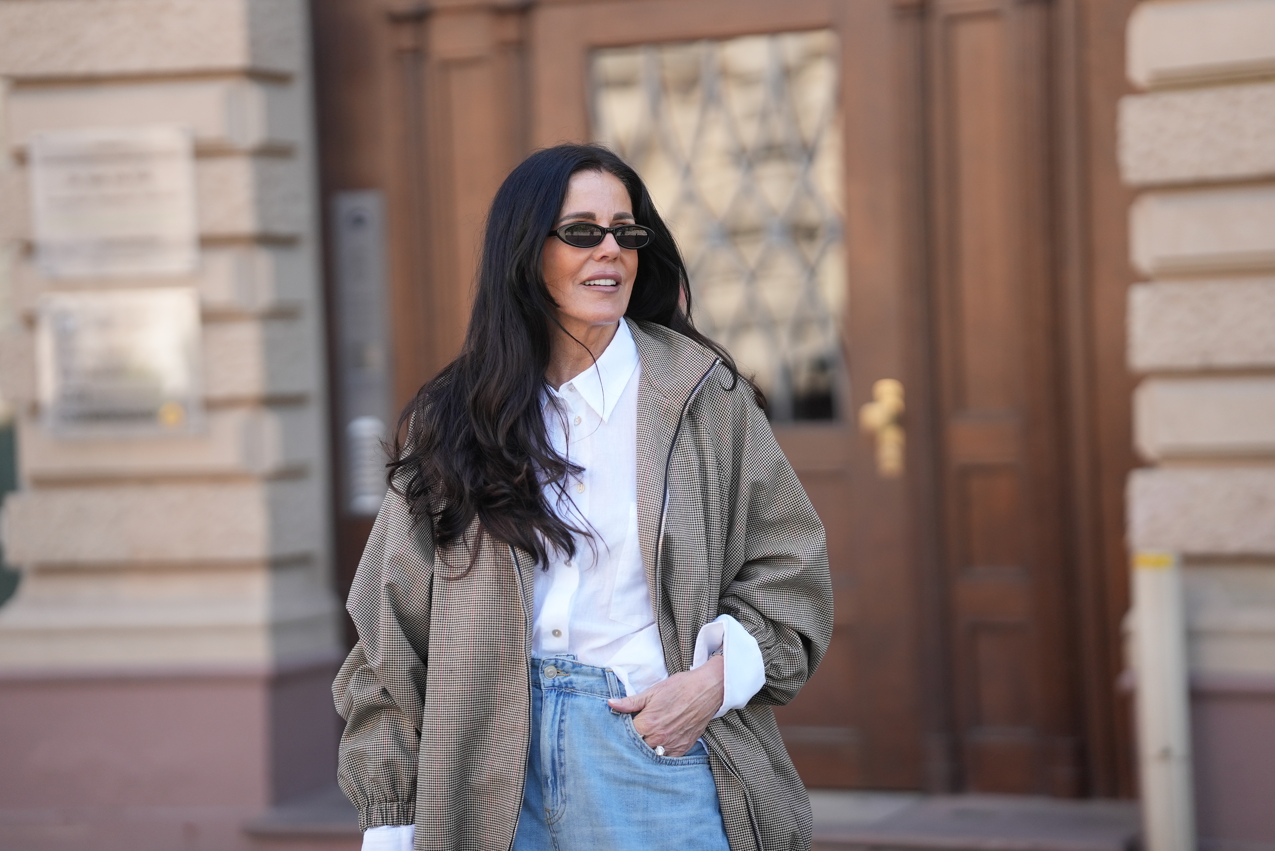 Angelika Hanel is seen wearing an oversized camel brown &bdquo;Baxter&ldquo; bomber jacket in a micro houndstooth check pattern with a zip fastening, dropped shoulders, wide elasticated hem and cuffs and a voluminous silhouette from The Frankie Shop; a white classic button down shirt with a point collar and wide statement cuffs visible at the sleeves from Zara; light blue wide leg barrel fit jeans from Zara; slim oval acetate sunglasses with a narrow black frame and dark tinted lenses from H&M; a natural manicure; small golden hoop earrings; her long dark brown hair is worn loose and wavy with a center part; with a natural make up look on April 22, 2026 in Frankfurt am Main, Germany.