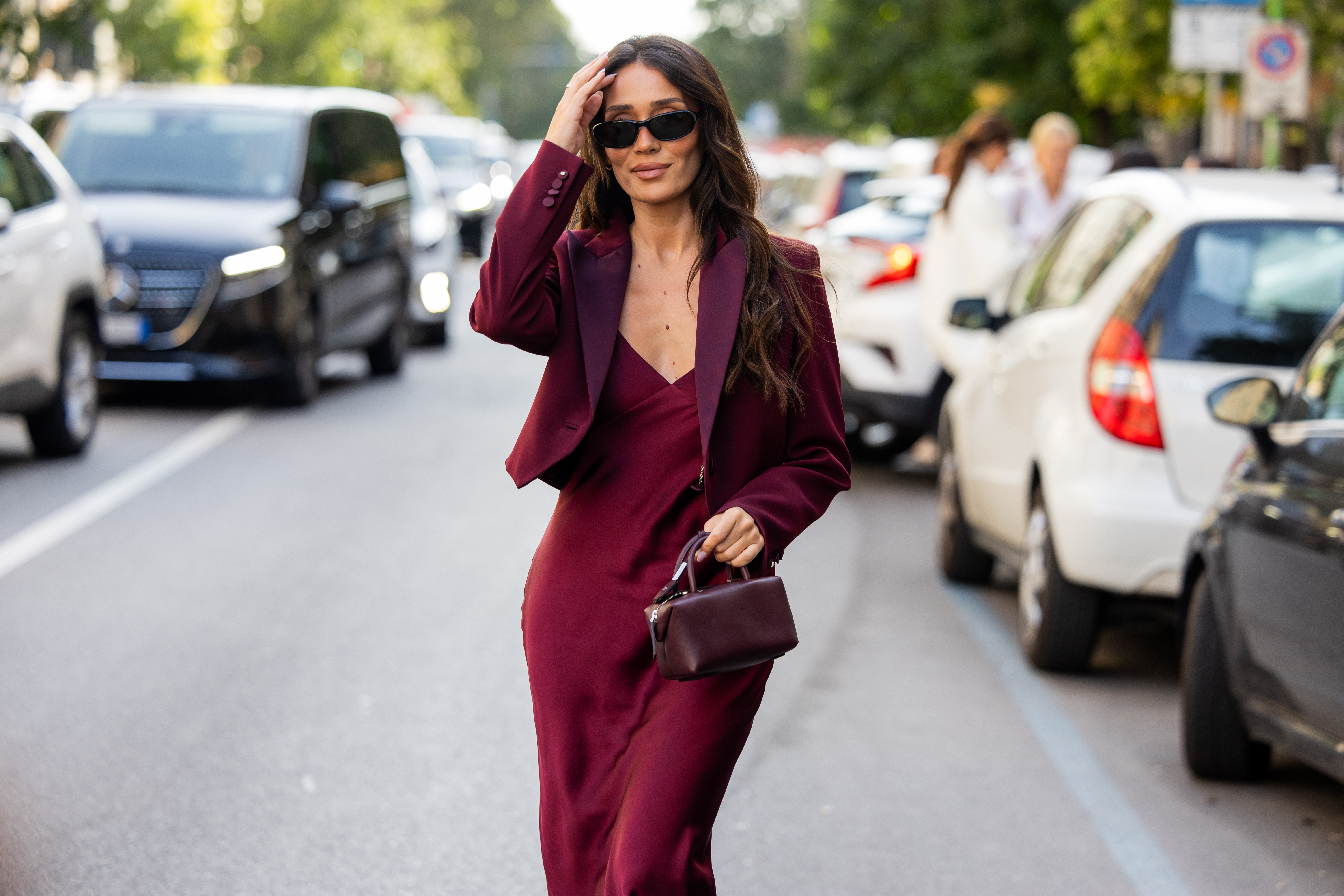 A guest wears a maroon cropped blazer with satin lapels, a matching slip dress a small maroon handbag outside Max Mara on September 24, 2026 in Milan, Italy.