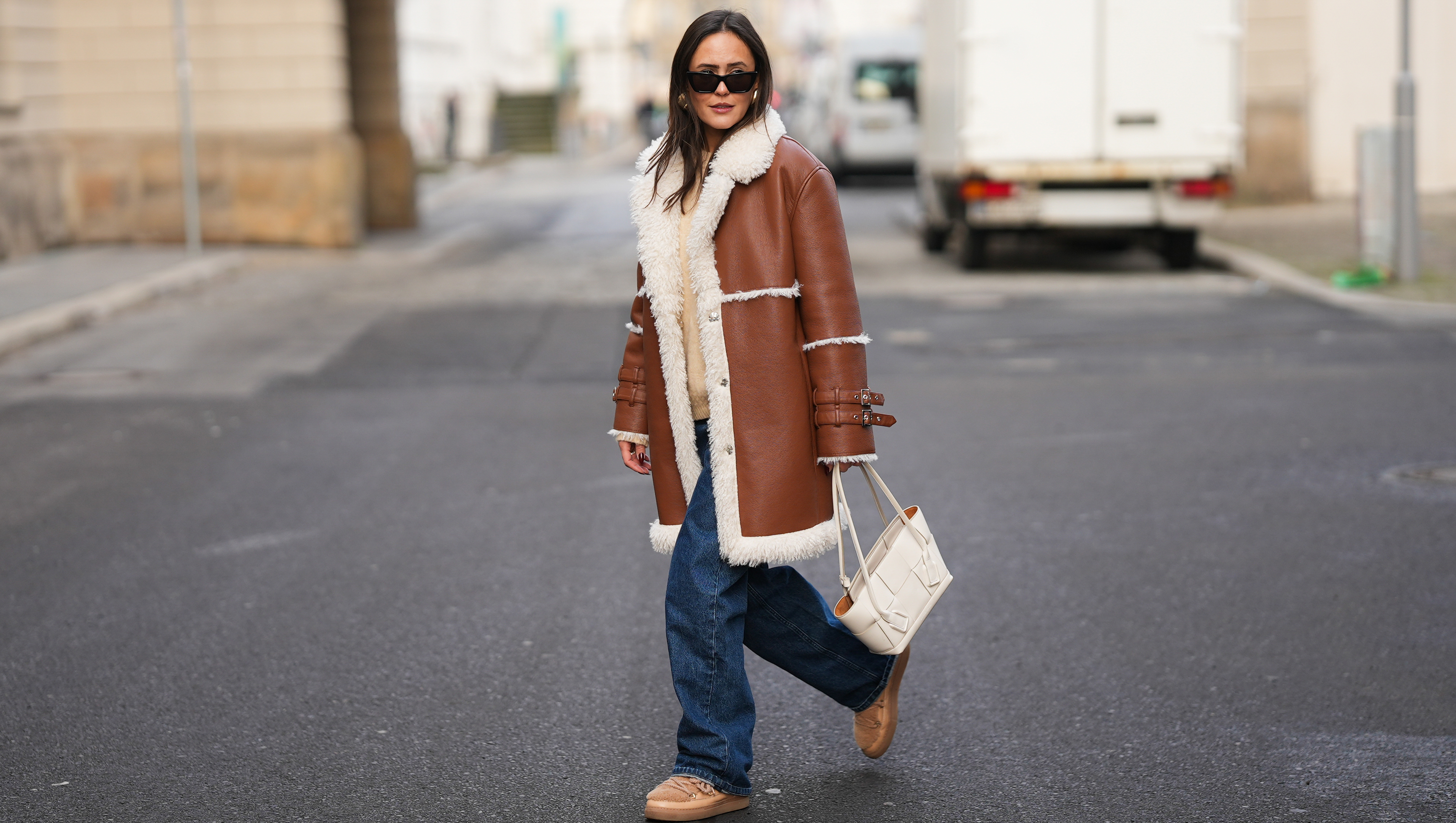 BERLIN, GERMANY - NOVEMBER 25: Laura Noltemeyer is seen wearing a shearling lining coat in a rich cognac tone with an oversized straight silhouette, wide lapels and buckle-strap cuff detailing on the sleeves from Max&Co; layered underneath is a soft beige wool-blend knit sweater with a ribbed crew neckline and ribbed trims from S&eacute;zane; dark-blue straight-leg denim trousers with a classic fit from By Aylin Koenig; beige suede winter boots with a rounded toe, exposed stitching and shearling lining from Inuikii; a white structured leather top-handle bag in an intrecciato weave and trapeze silhouette called &ldquo;Intrecciato Tote&rdquo; from Bottega Veneta; chunky sculptural gold earrings from Zara; black angular acetate sunglasses with a thick frame and dark lenses from Saint Laurent; her dark-brown hair is worn straight with a center part on November 25, 2025 in Berlin, Germany. (Photo by Moritz Scholz/Getty Images)